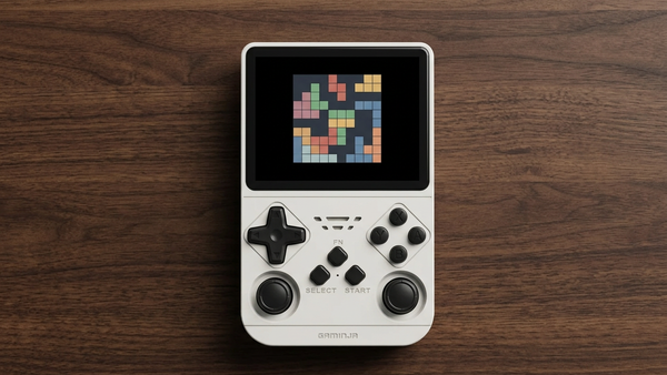 Editorial illustration of a white ANS11-style handheld on a desk with original pixel-block art